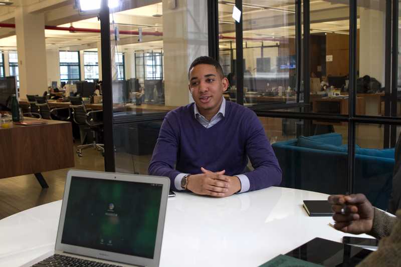 a man sitting in meeting room at small desk in front of two people interviewing for a job