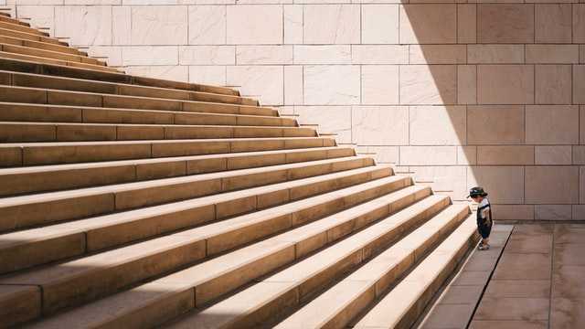 side view of young child standing in front of a large set of stairs symbolizing a large challenge to accomplish